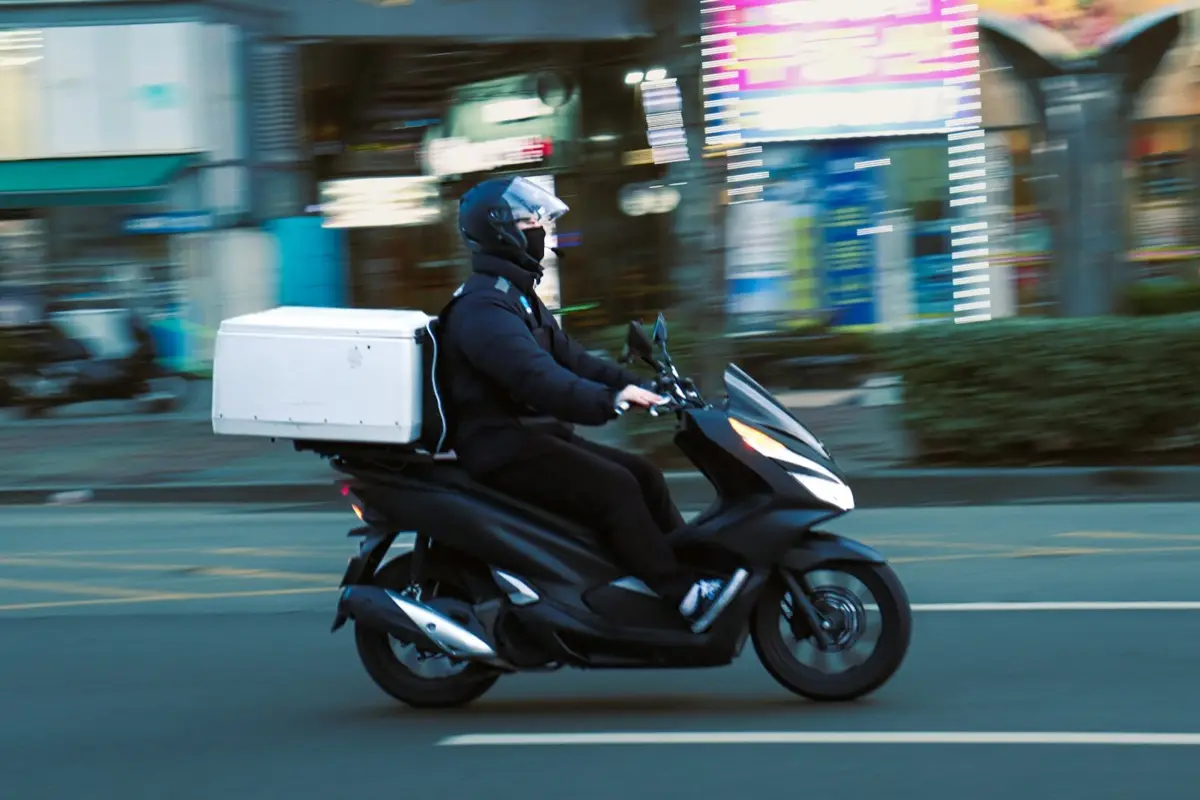 Two hands passing paper takeaway bags with a red sticker, outdoors